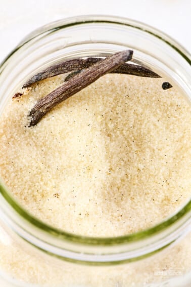 Vanilla beans and sugar in a glass container.