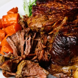 Pot roast on a white platter with vegetables and rosemary.