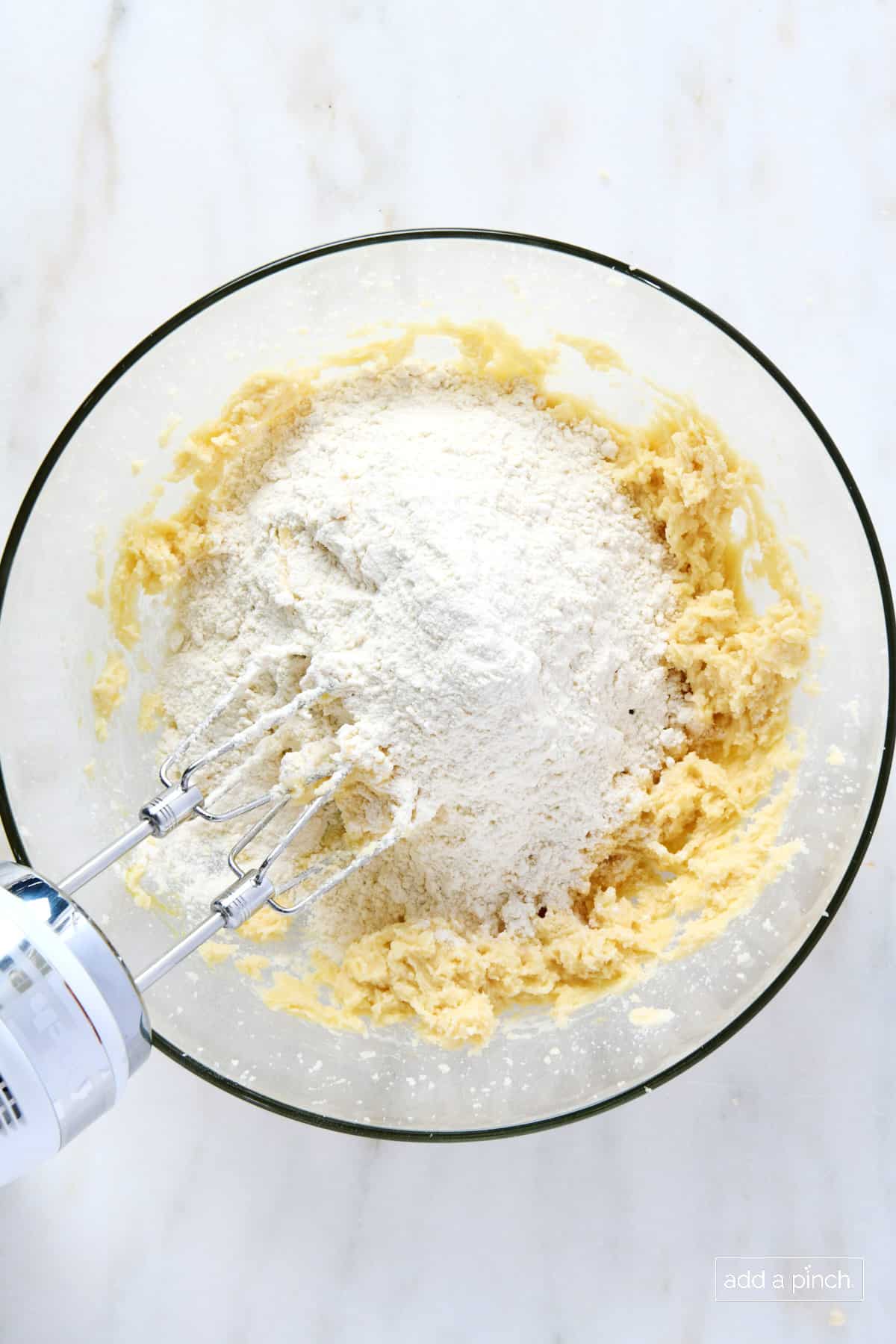 Flour added to cookie dough mixture in a glass bowl with a hand mixer.