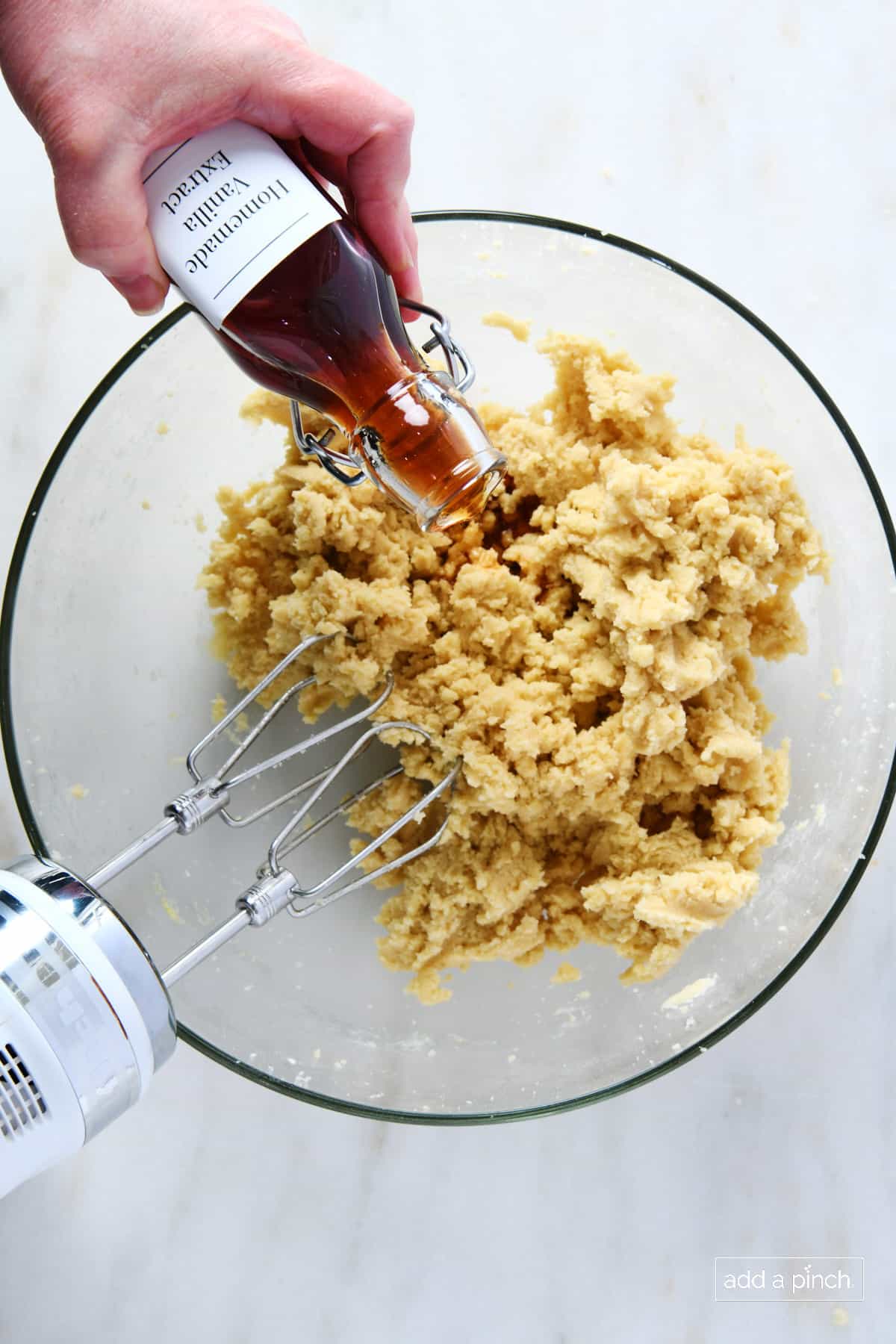 Vanilla extract being added to cookie dough mixture in a glass bowl with hand mixer.