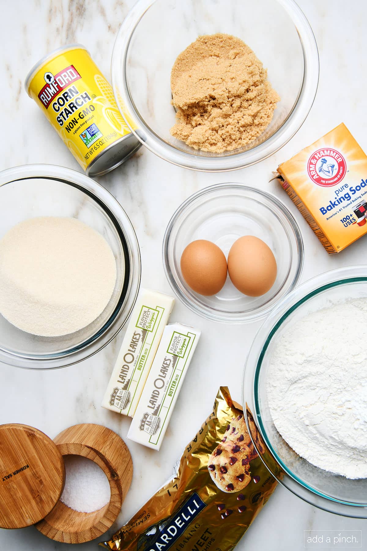 Ingredients for Chocolate chip cookie cake: flour, salt, baking soda, eggs, butter, granulated sugar, brown sugar, and corn starch on a marble countertop.