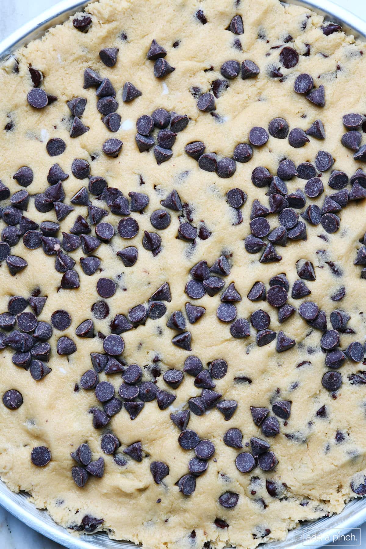 Cookie cake dough is pressed into cake pan. Chocolate chips are sprinkled on top of dough.