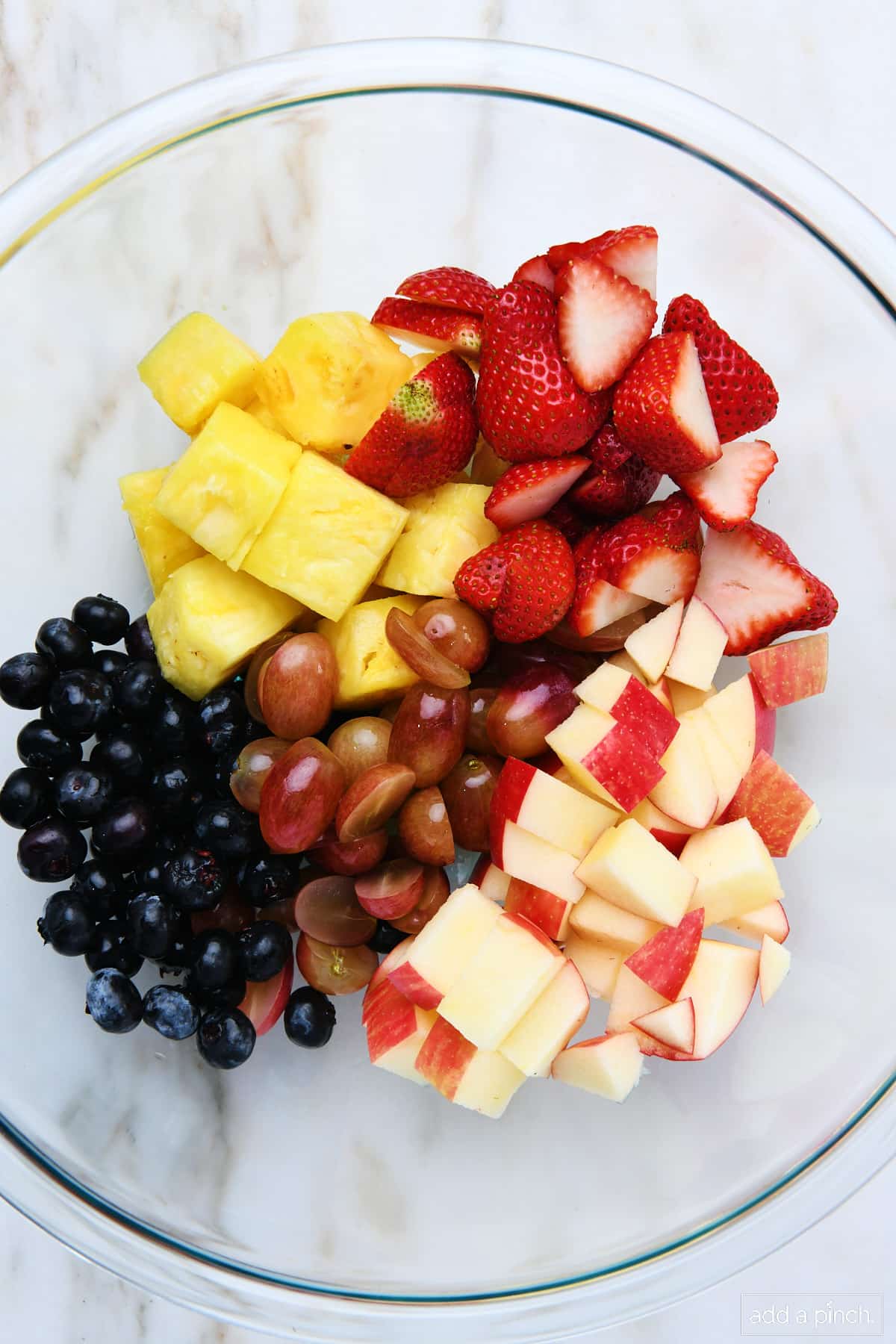 Cut fresh fruit in a glass bowl on a marble counter.
