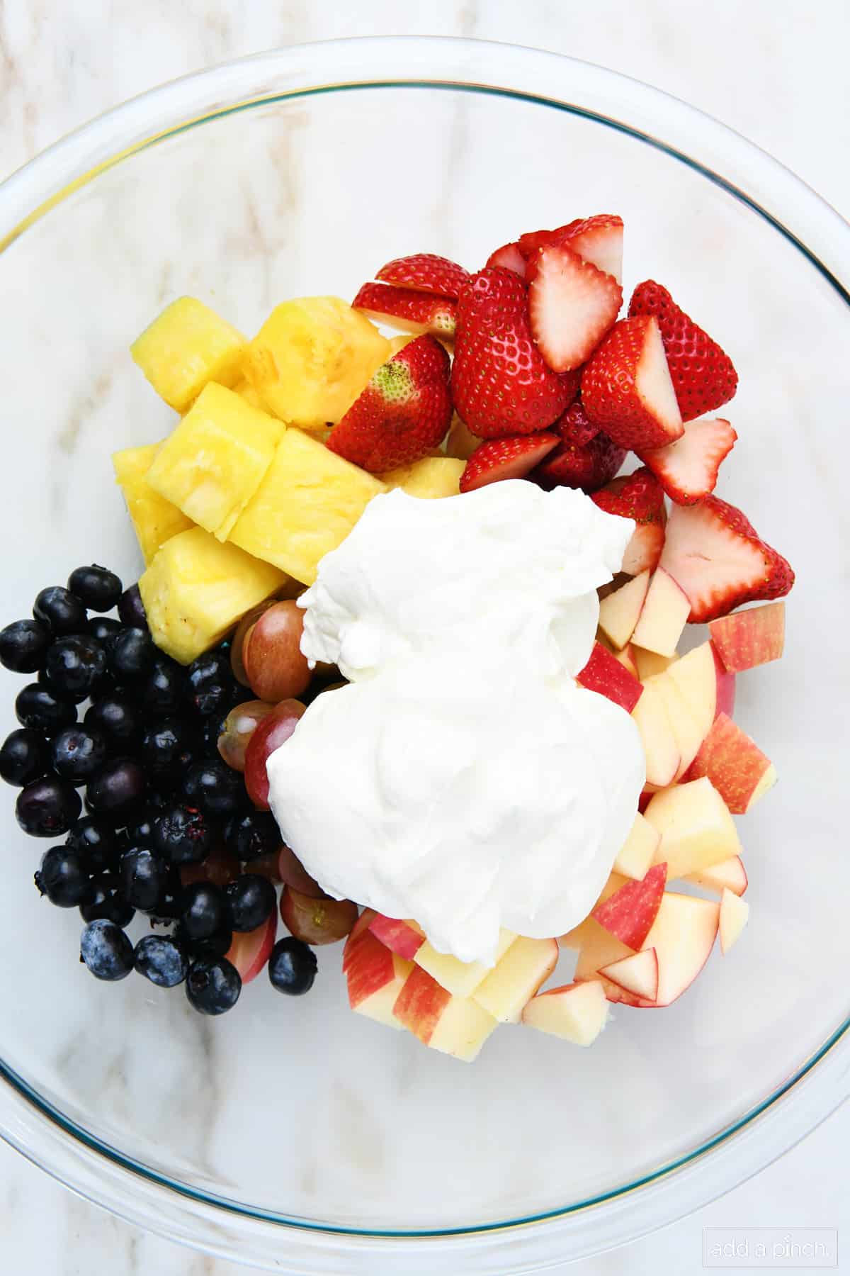 Fresh fruit topped with creamy dressing in a glass bowl.