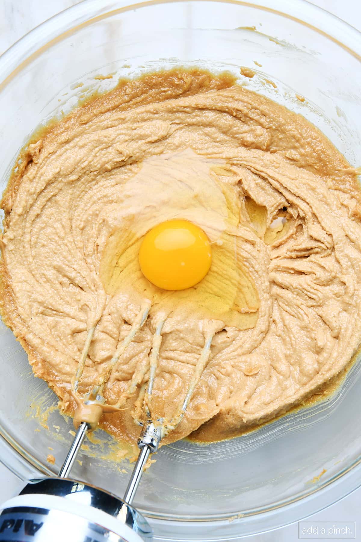 Creamed peanut butter and sugar mixture with egg in a mixing bowl.