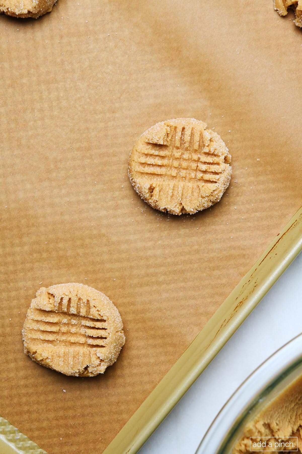 Parchment-lined baking sheet with peanut butter cookies with criss cross pattern on the top, placed a few inches apart and ready to bake. 
