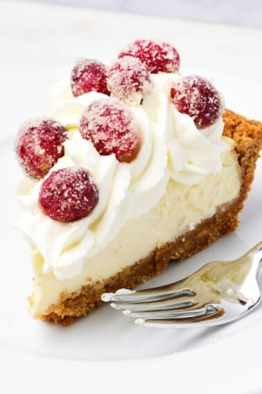 A slice of cheesecake pie topped with whipped cream and sugared cranberries on a white plate.