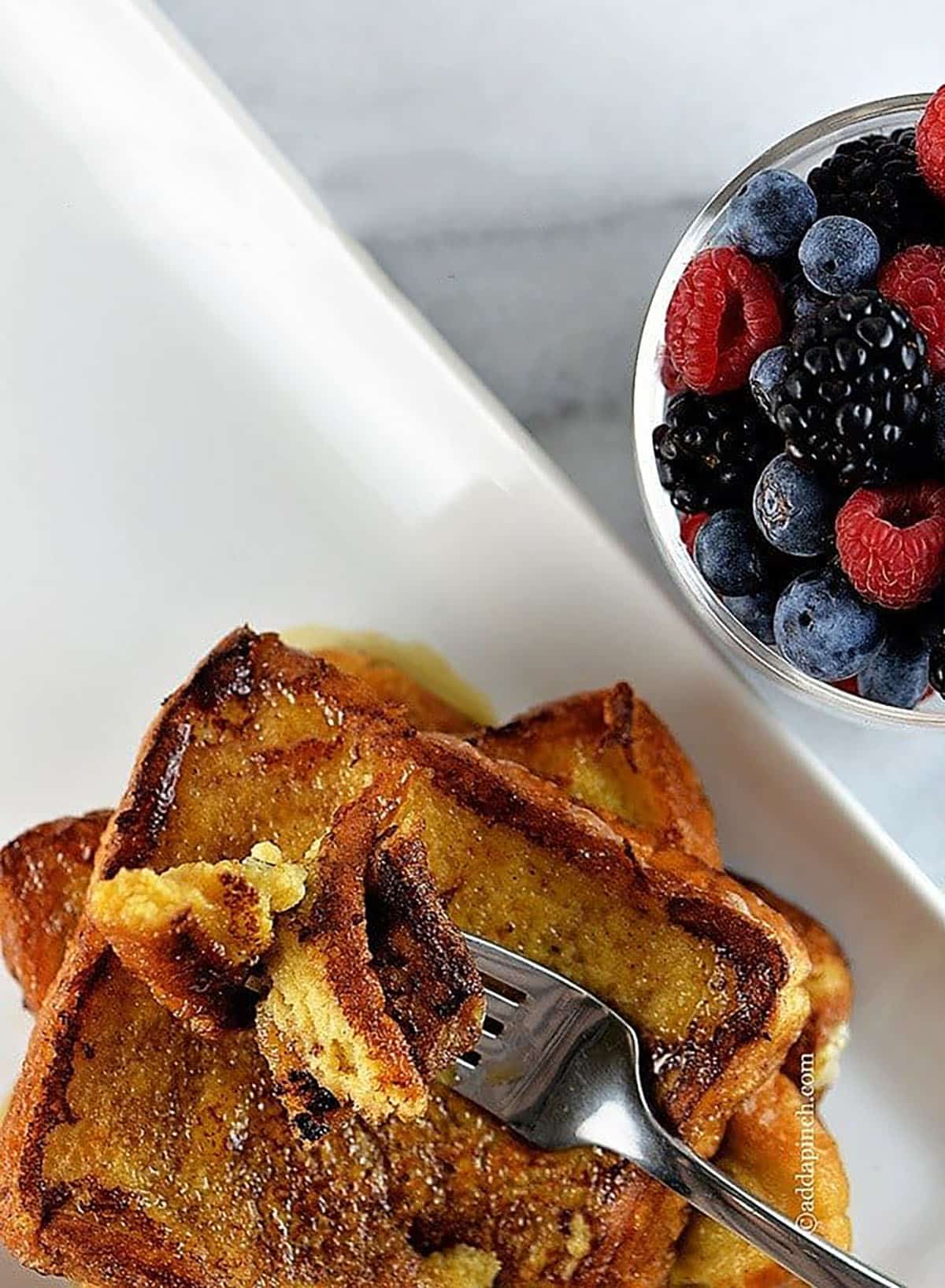 Overhead photo of plate of French toast and a glass bowl on the side with fresh berries.