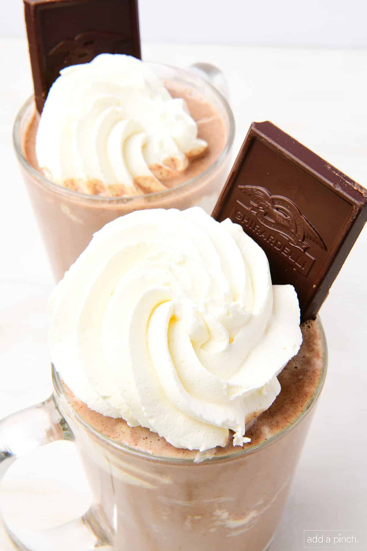 Mugs filled with hot chocolate and whipped cream, and a chocolate bar for garnish.