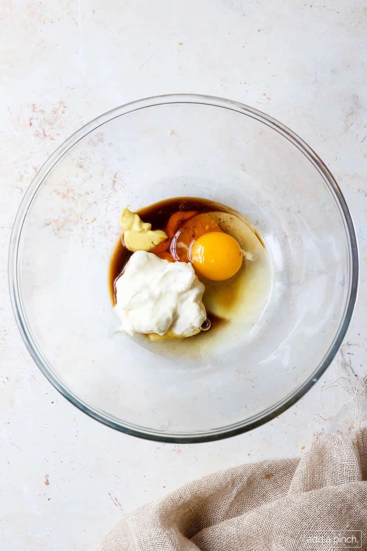 Mayo, dijon mustard, egg, and sauces in a glass bowl.