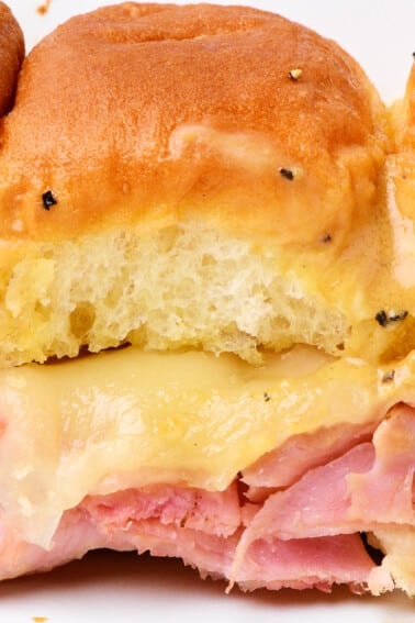 Hot ham and cheese sliders on a white plate.