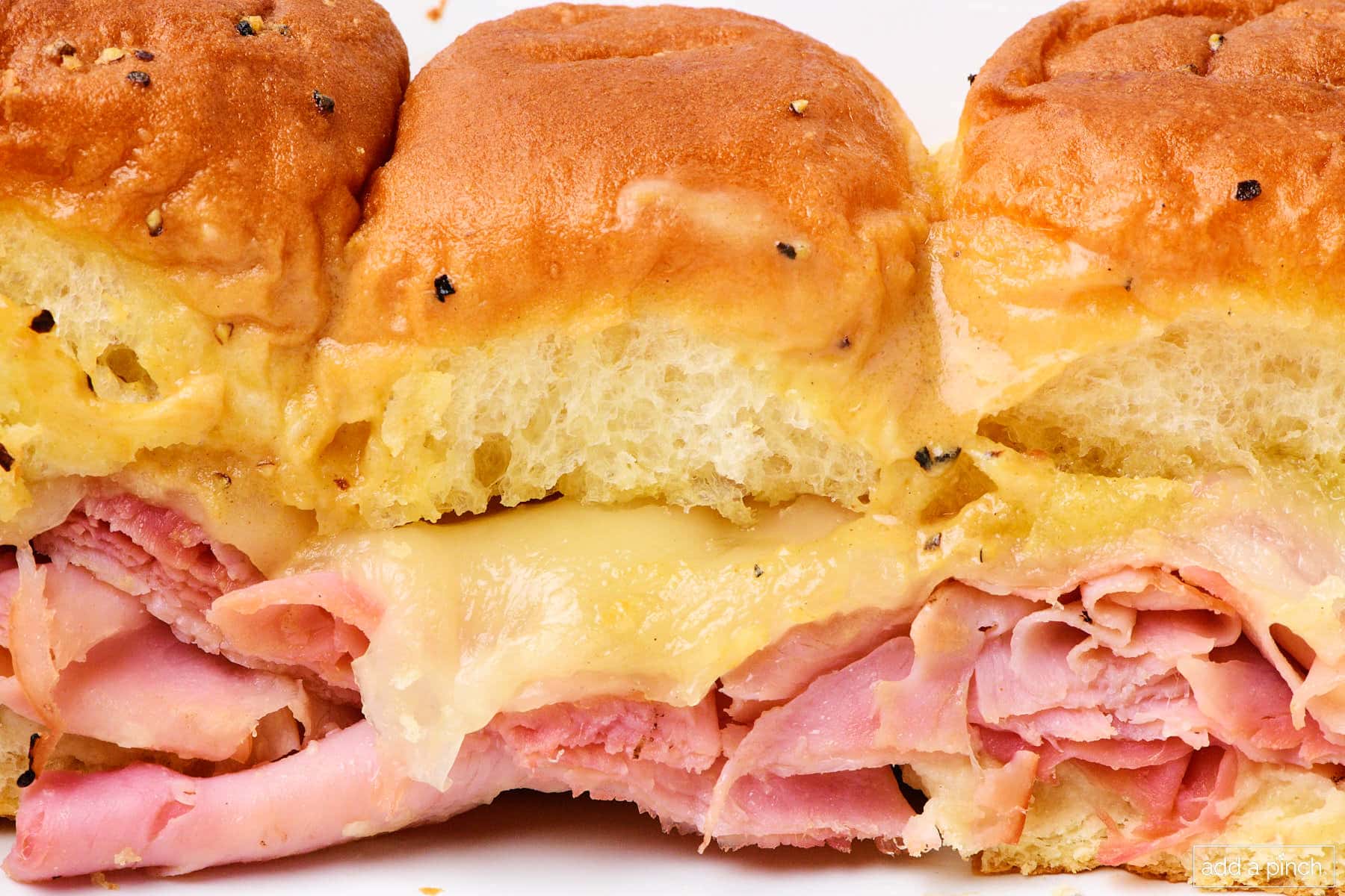 Hot ham and cheese sliders on a white plate.