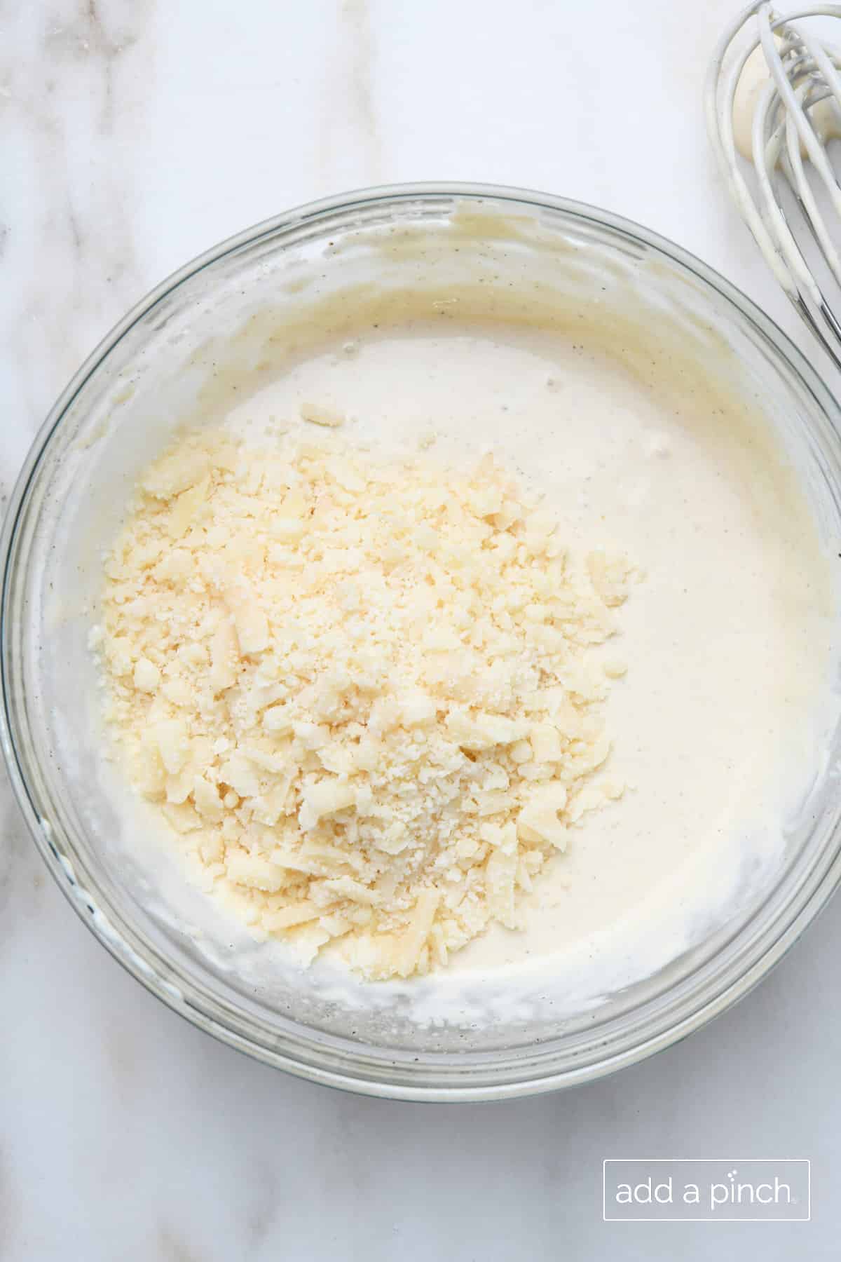 Parmesan cheese added to Caesar dressing in a glass bowl.