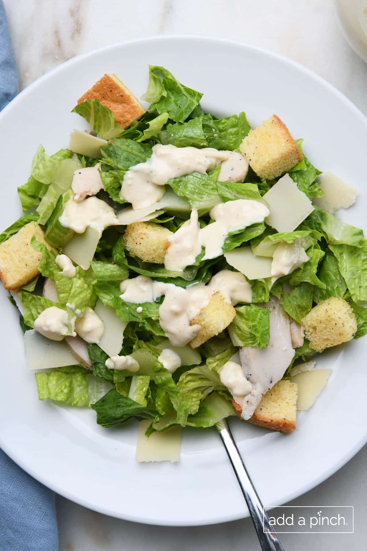 Caesar salad topped with Caesar dressing on a white plate.