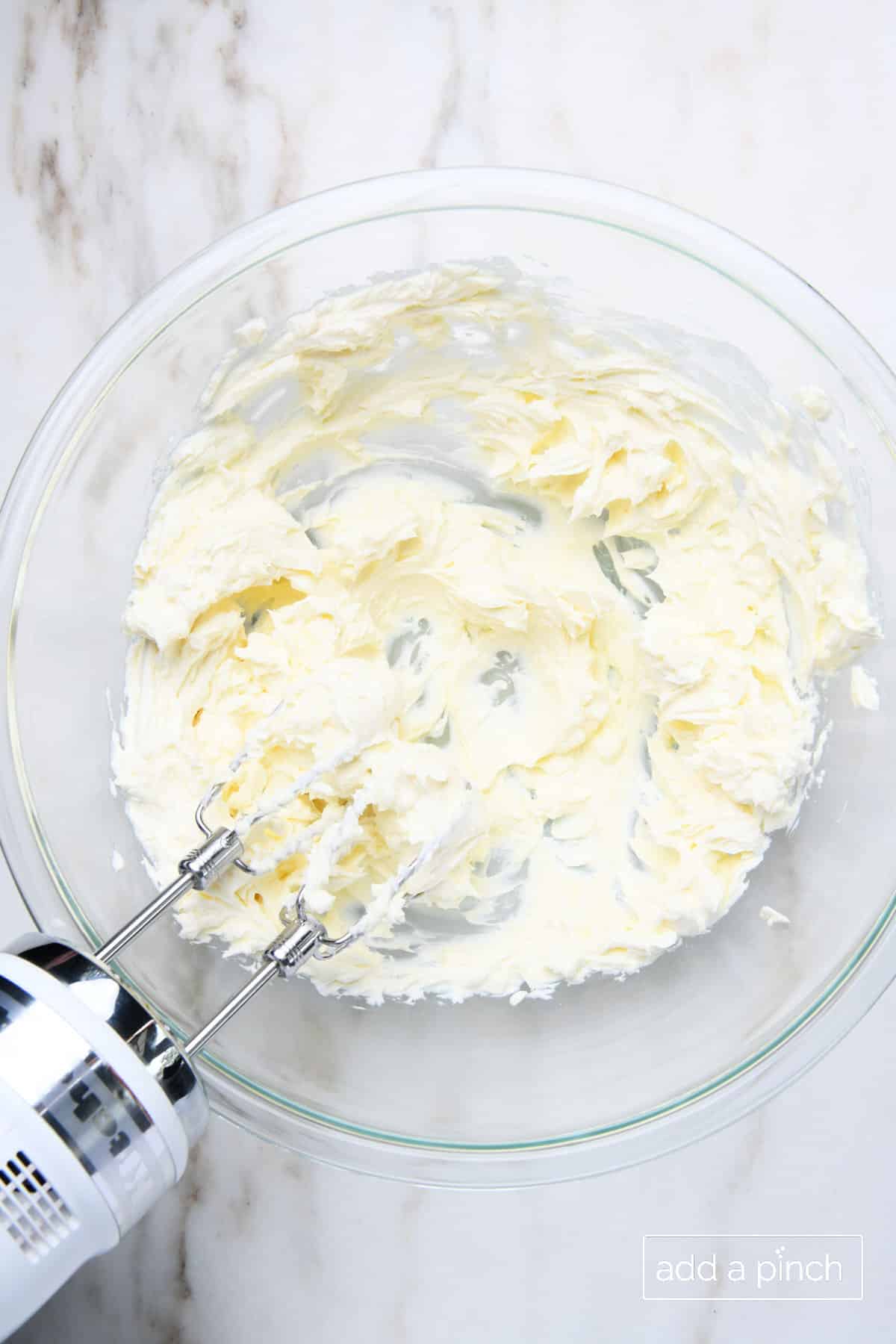 Cream cheese and butter are creamed together with hand mixer in glass mixing bowl.