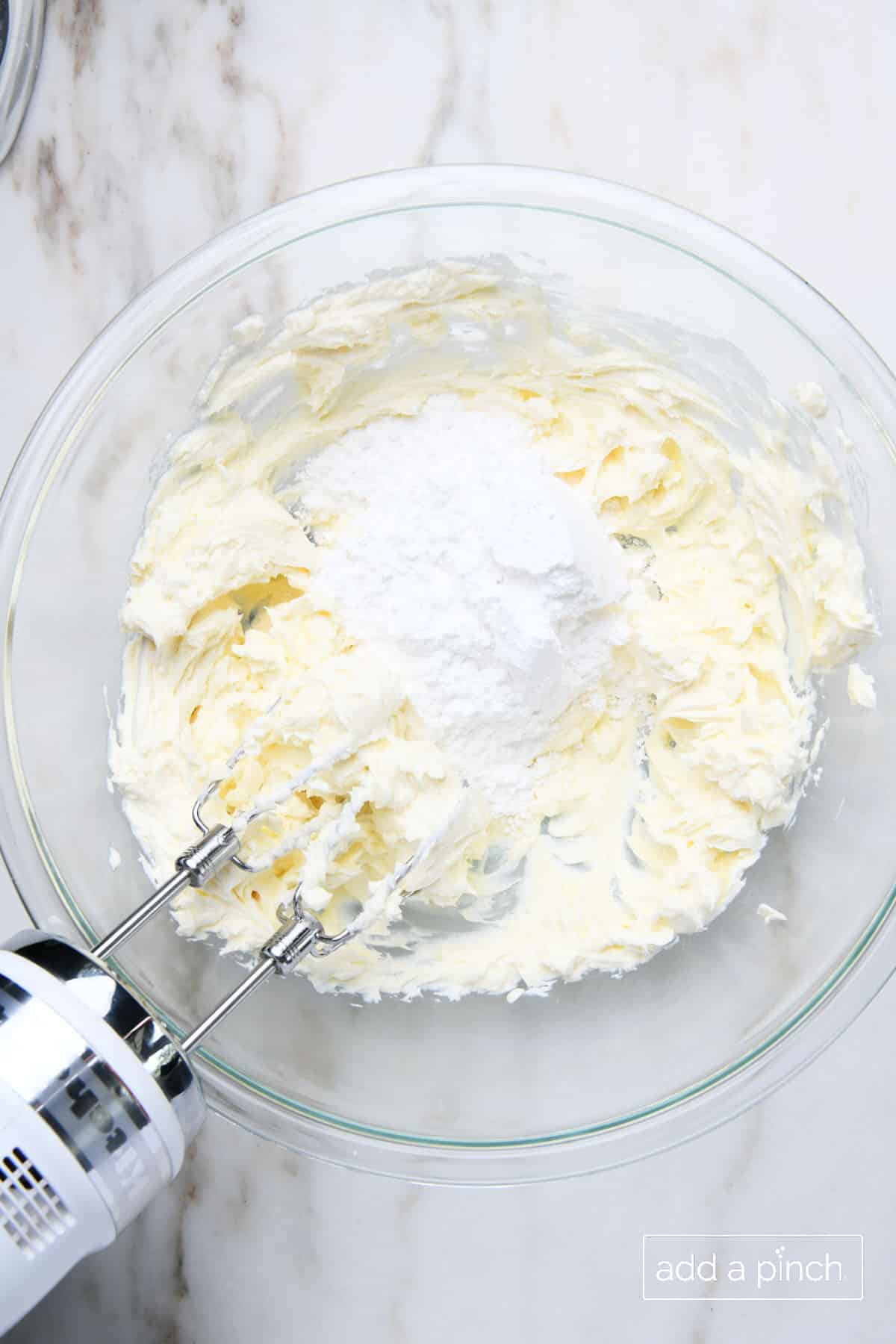 Glass mixing bowl with smooth cream cheese and butter with powdered sugar added.