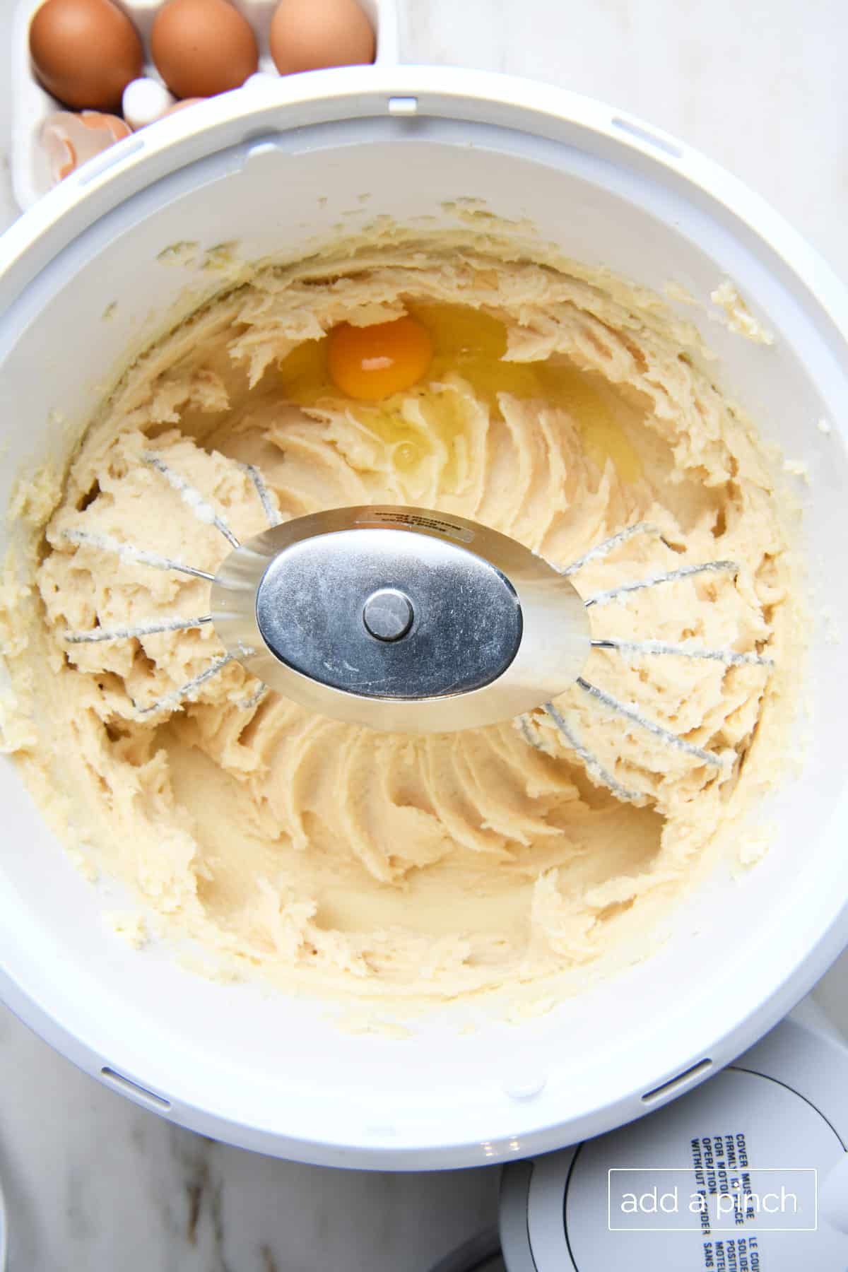 Stand mixer bowl holds butter, cream cheese and sugar that's been creamed together and an egg about to be mixed in with it. 