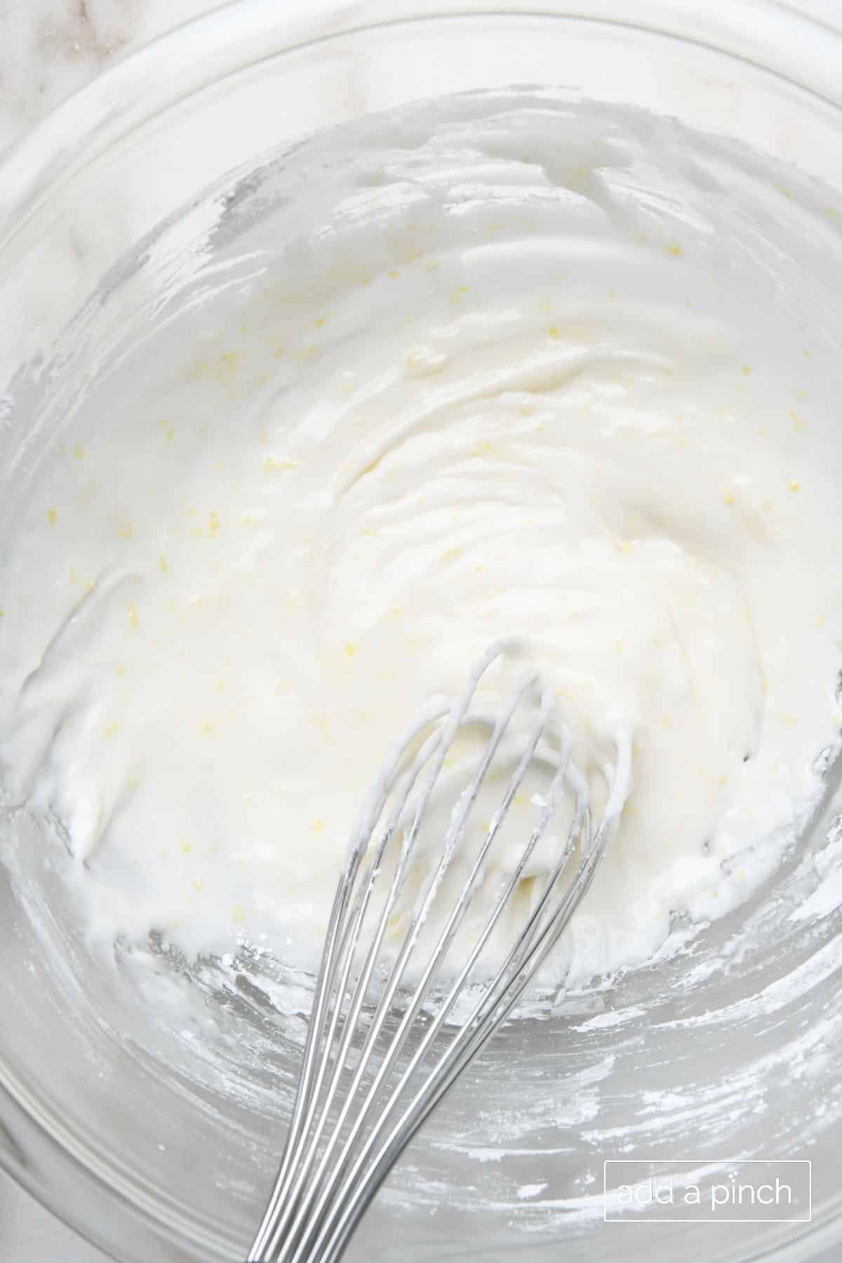A wire whisk whips together the ingredients for the lemon buttermilk glaze in a glass mixing bowl.
