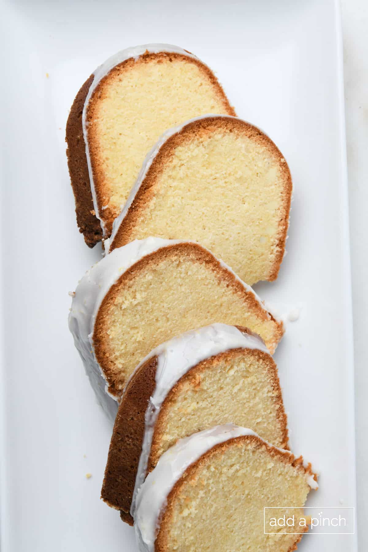 Five slices of glazed lemon pound cake sit on a white tray.