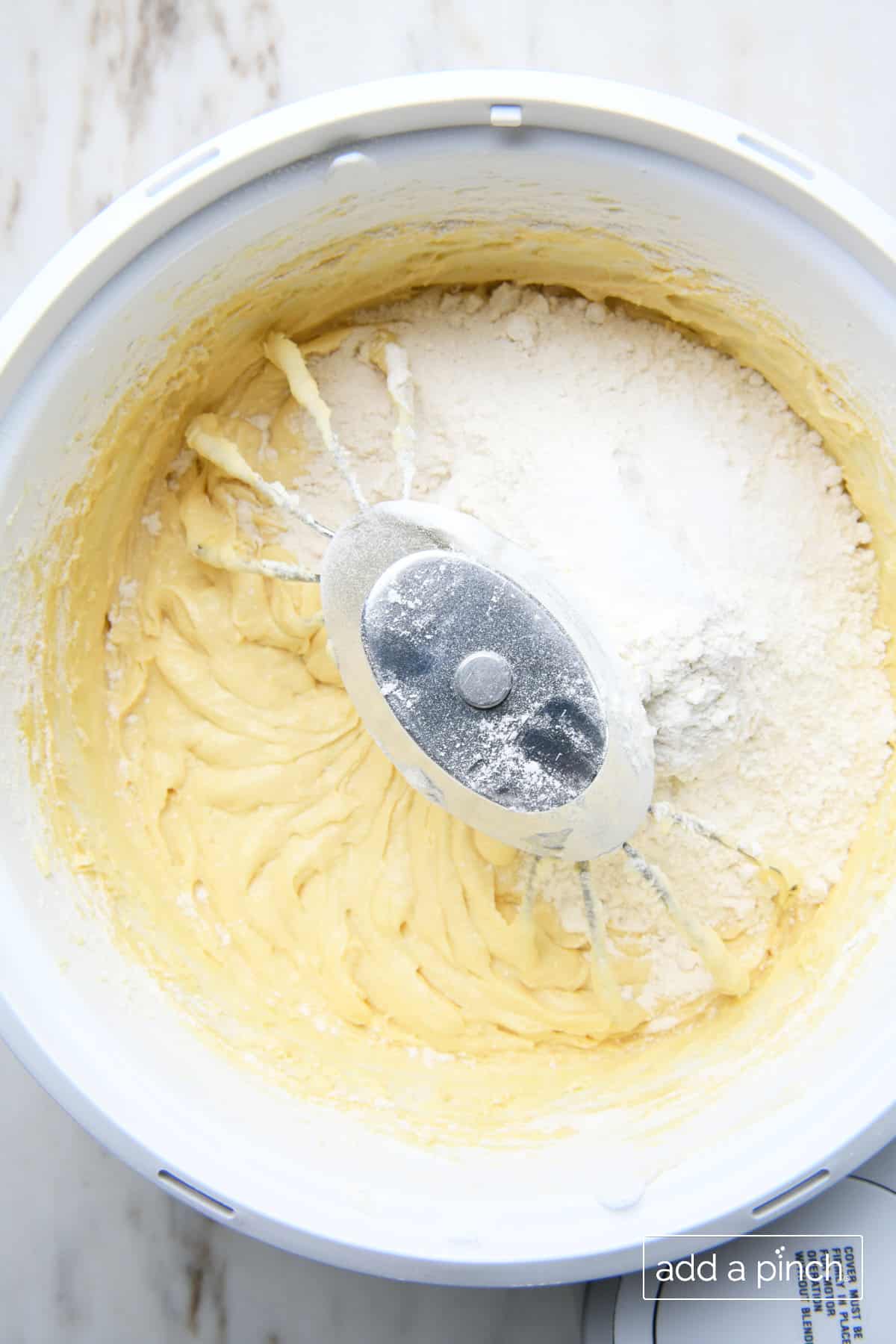 Flour is slowly added to other mixed lemon pound cake ingredients in the mixing bowl of a stand mixer.