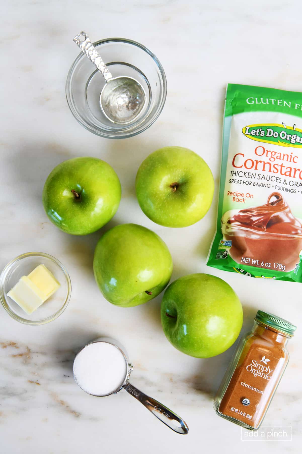 Apples, sugar, butter, cinnamon, corn starch and water on a marble counter ready to make Apple Pie Filling.