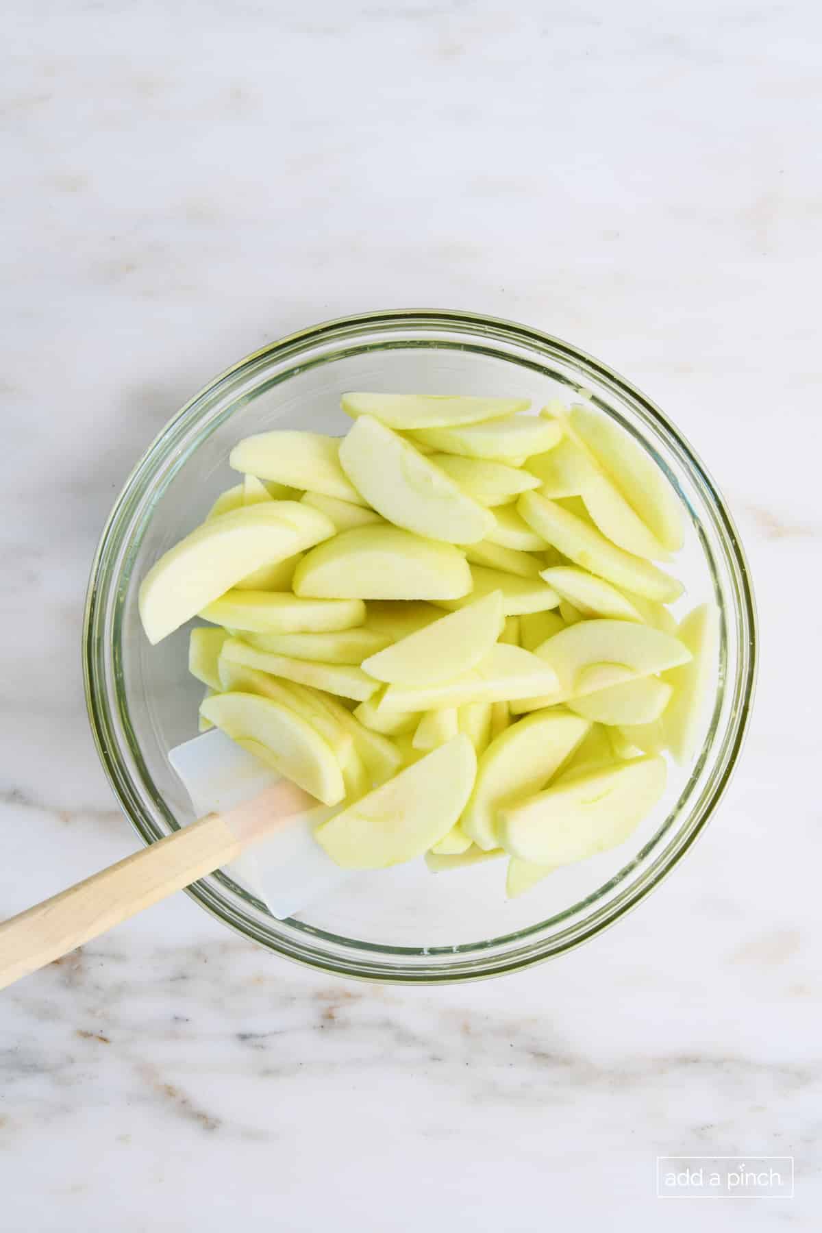 Sliced apples in a glass bowl on a white marble counter. 