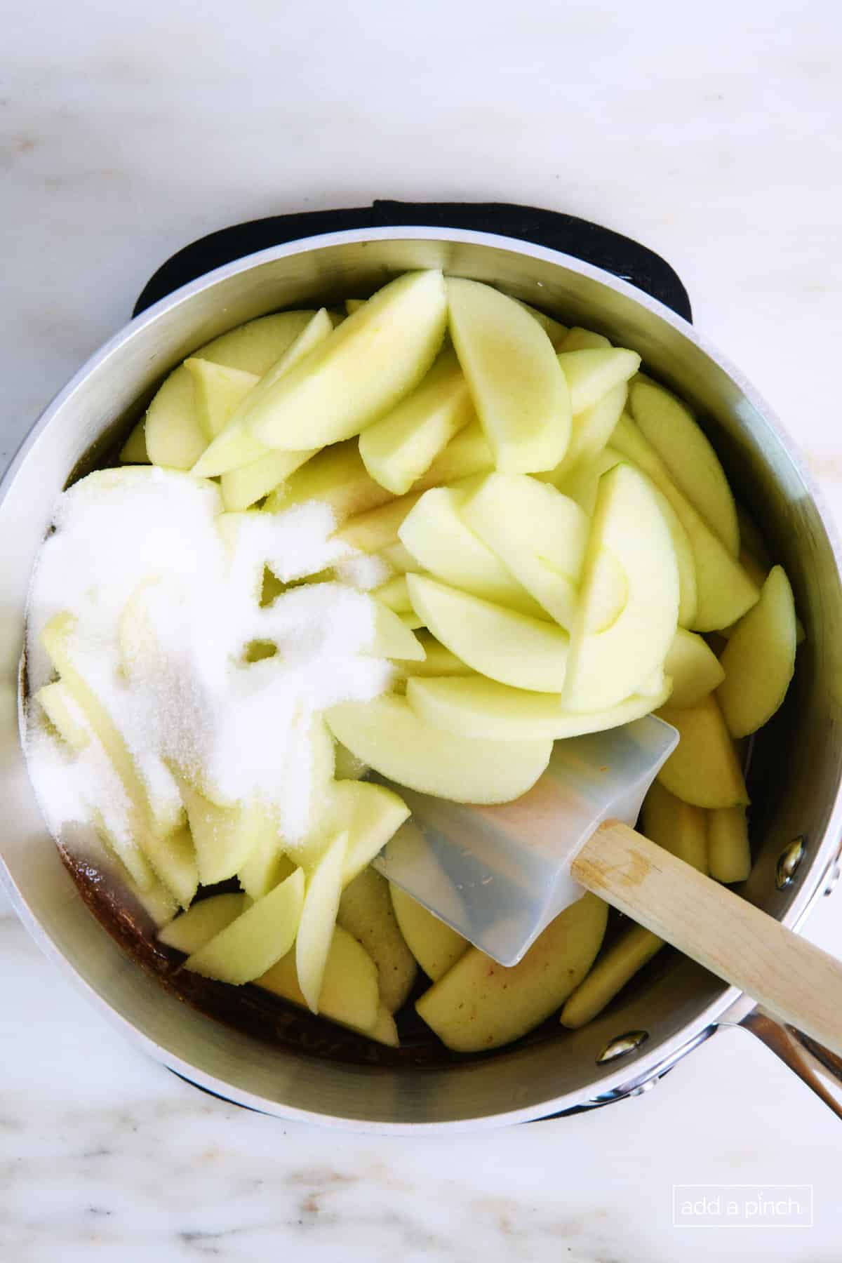 Saucepan holds cinnamon sauce mixture along with sliced apples and white sugar. 