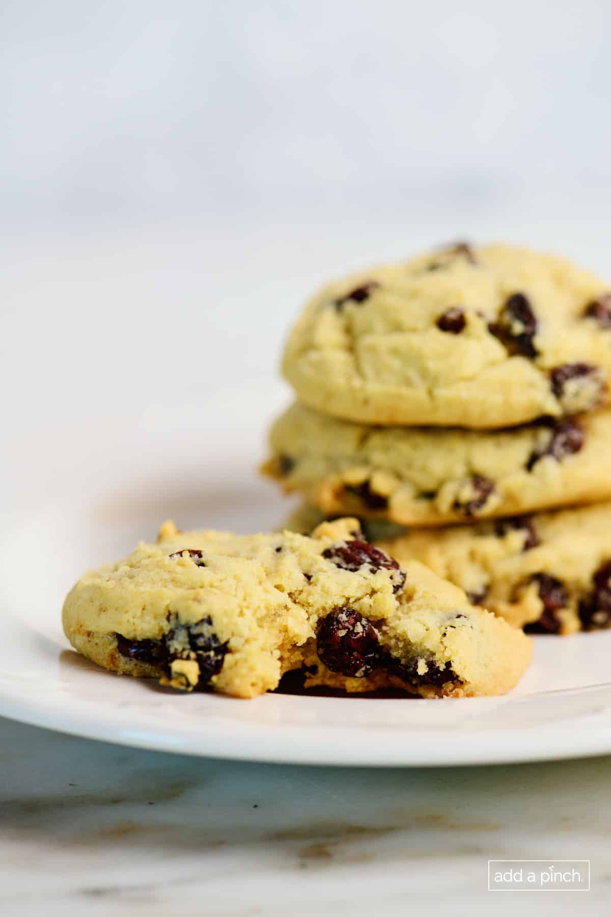 Stack of oatmeal raisin cookies with one bitten on a white plate. 