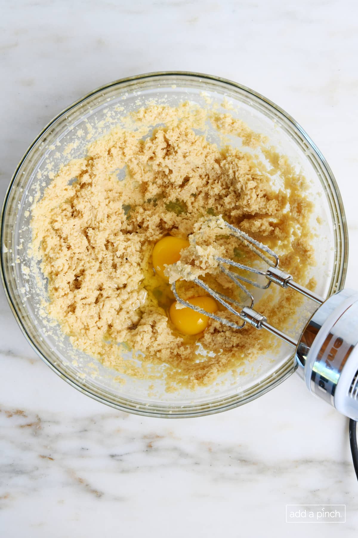 Eggs are beaten into the butter mixture with a hand mixer for Oatmeal Raisin Cookies.