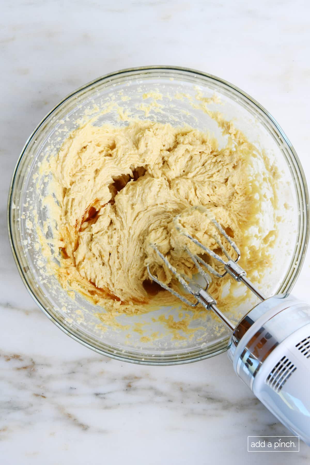 Vanilla extract is mixed into wet ingredients for cookie dough with a hand mixer.