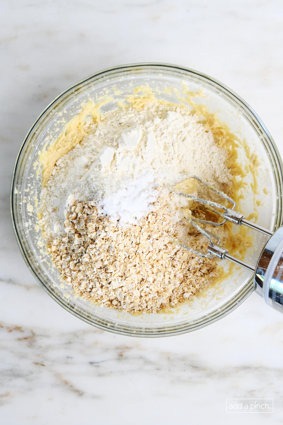 Dry ingredients of flour, baking soda, salt and quick oats are added to glass bowl with wet ingredients and mixed with a hand mixer. 