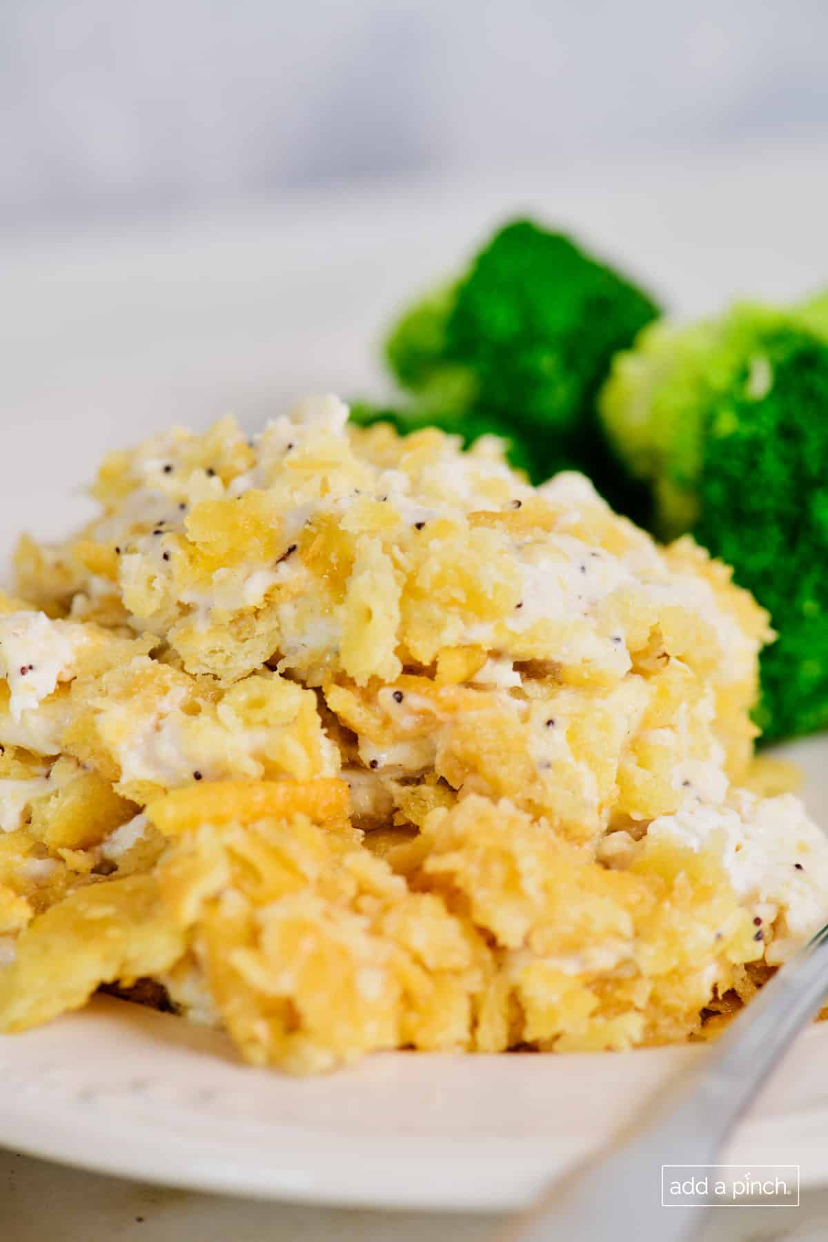 Golden brown topped Poppy Seed Chicken Casserole served on a plate with broccoli. 