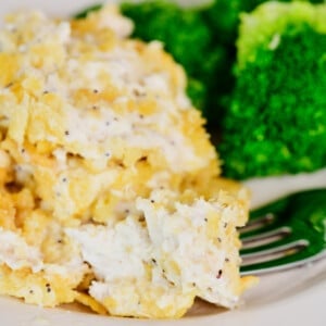 A bite of chicken on a fork from Poppy Seed Chicken Casserole. Broccoli is on the plate in the background