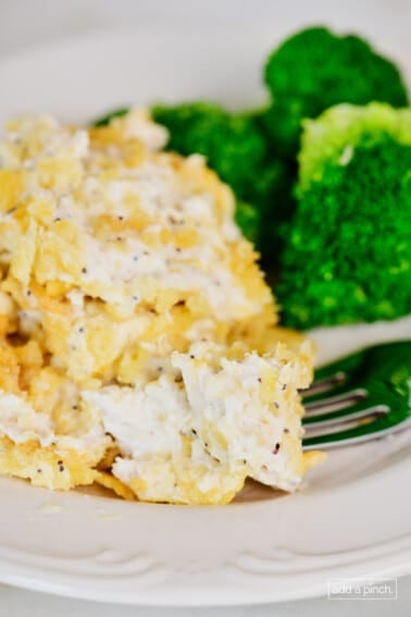 A bite of chicken on a fork from Poppy Seed Chicken Casserole. Broccoli is on the plate in the background