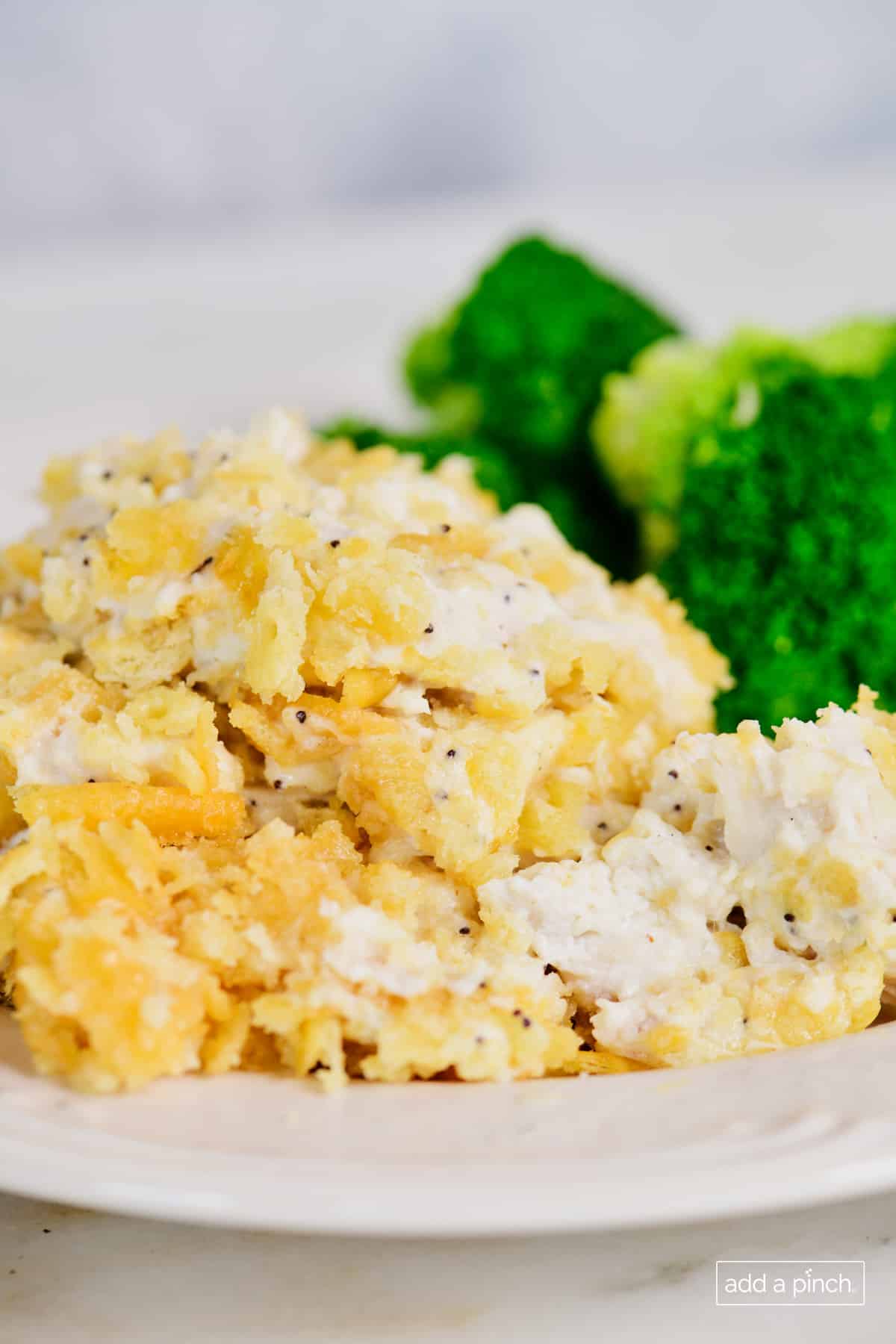 Chunks of shredded chicken show in Poppy Seed Chicken Casserole on a plate with broccoli.