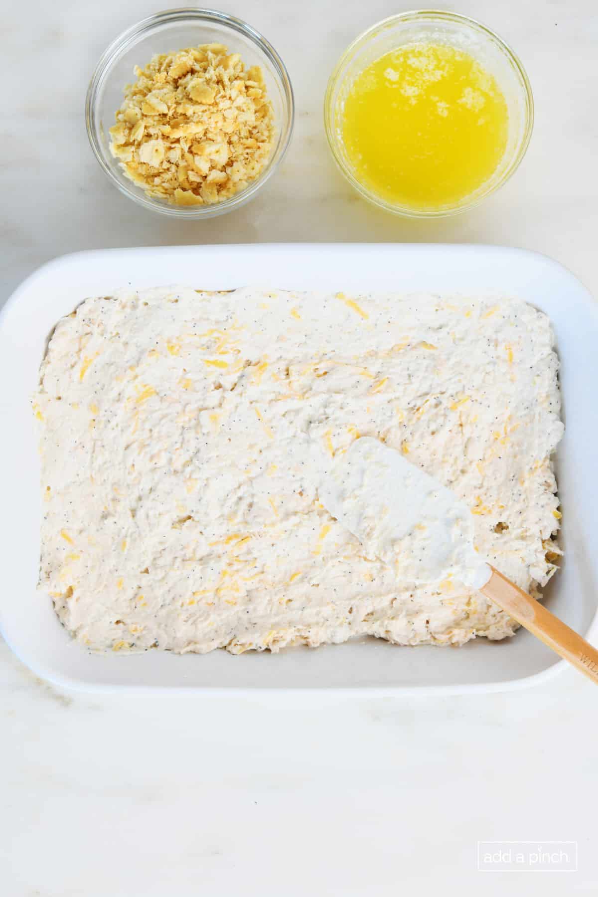 White ceramic baking dish holds the chicken casserole ingredients while a bowl of crushed crackers and melted butter sit to the side waiting to top the dish. 