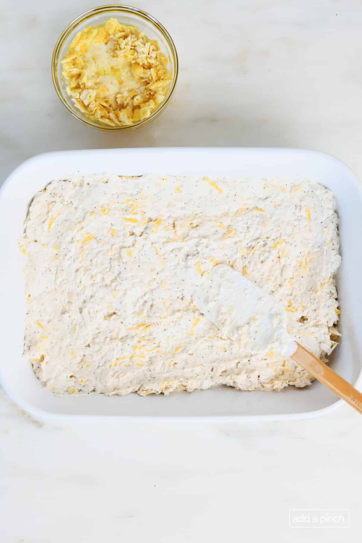 Crushed butter crackers and melted butter have been mixed and ready to be spread on top of poppy seed chicken casserole in white baking dish. 