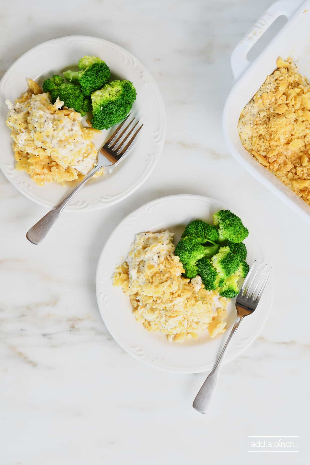 Two plates hold servings of poppy seed chicken casserole along with fresh steamed broccoli and forks.