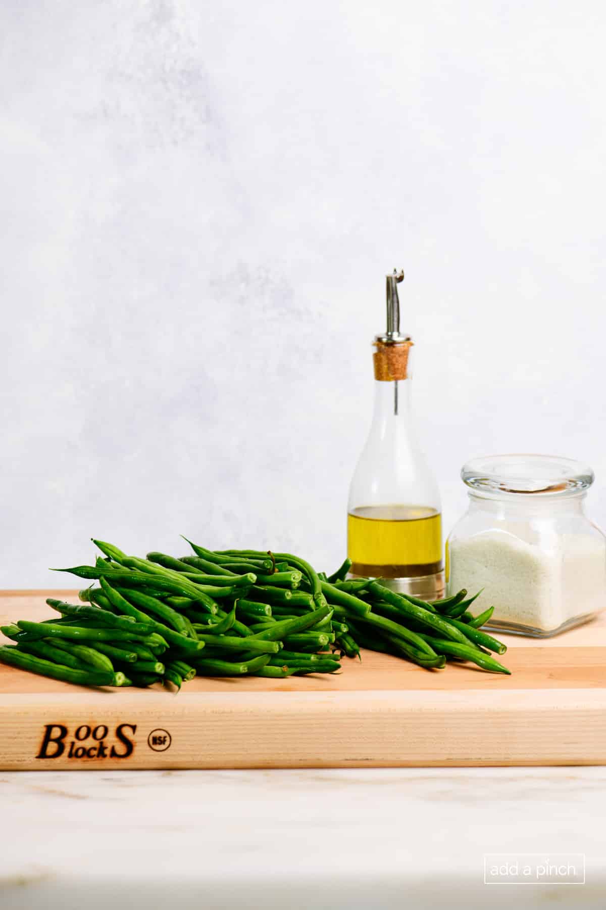 Wooden block holds fresh green beans, olive oil in a glass and pewter bottle, and salt in a glass container.