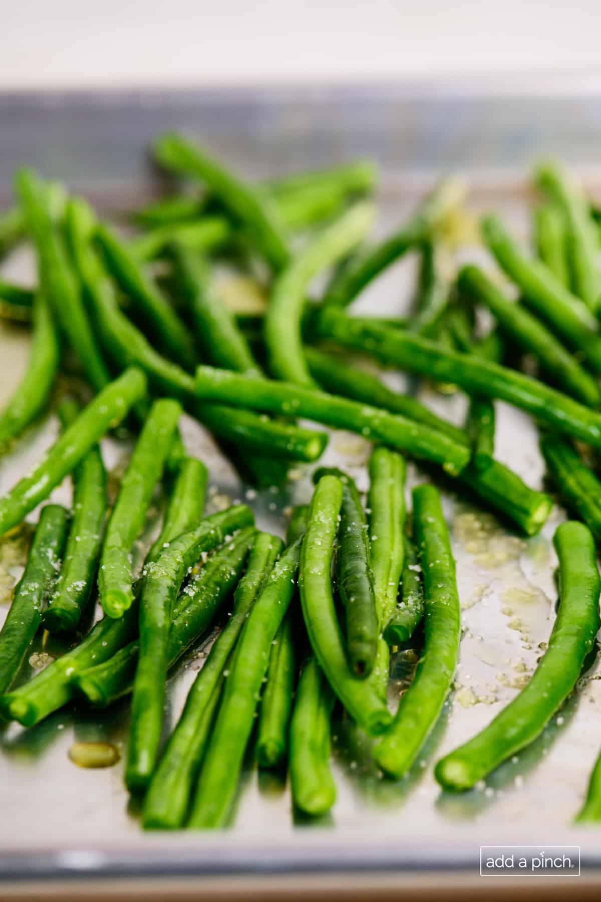 Fresh green beans drizzled with olive oil and sprinkled with salt on a baking sheet.