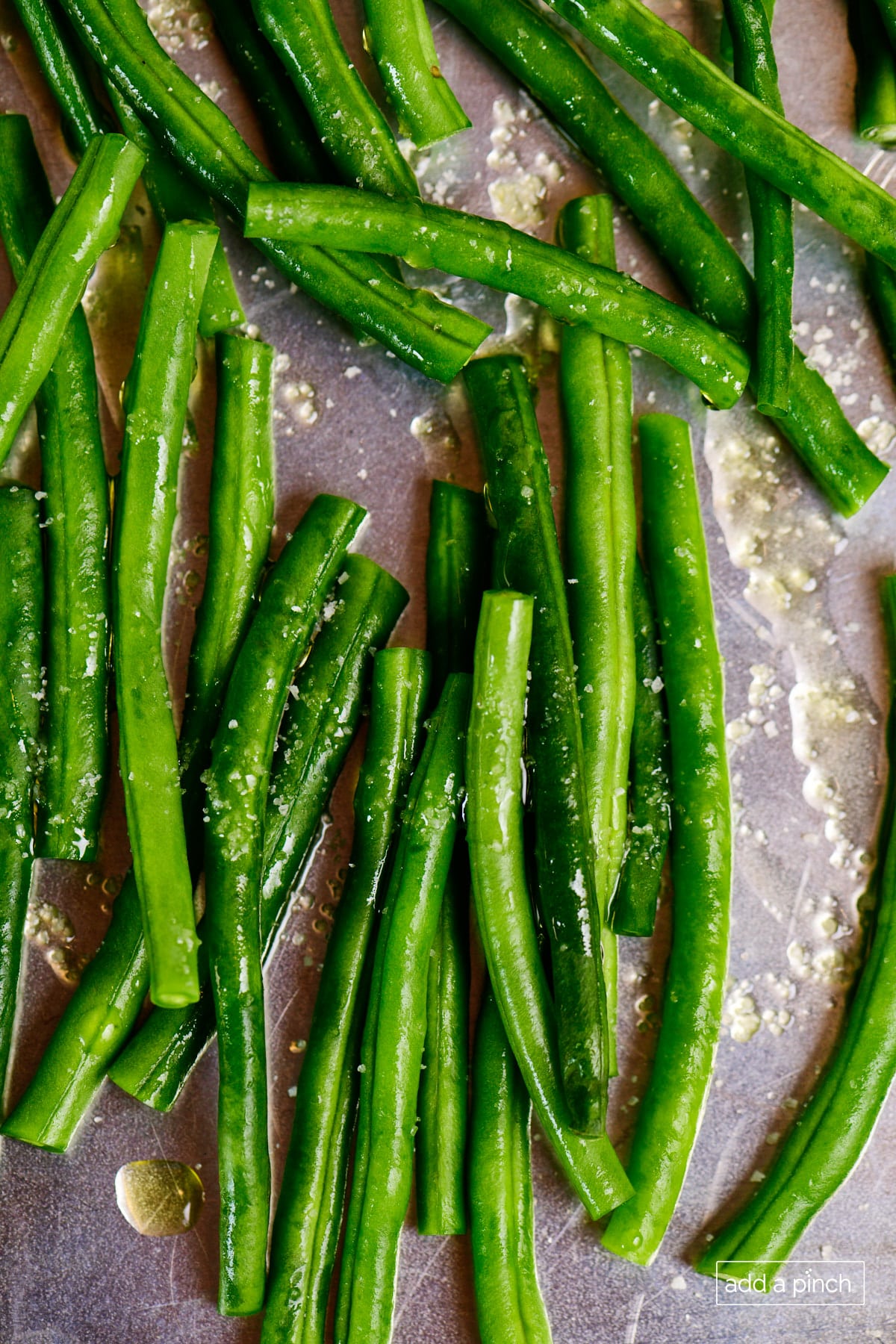 Fresh green beans on a baking sheet are tossed in olive oil and salt. 