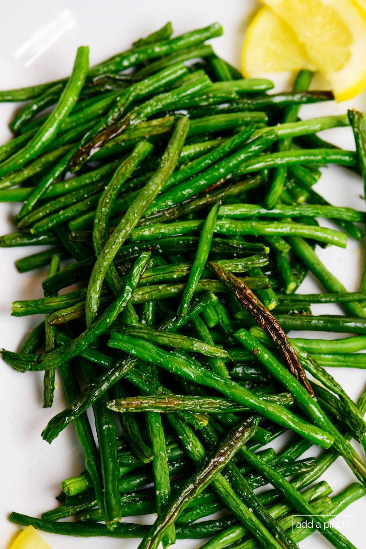 White plate with caramelized roasted green beans and lemon wedge on edge of plate. 