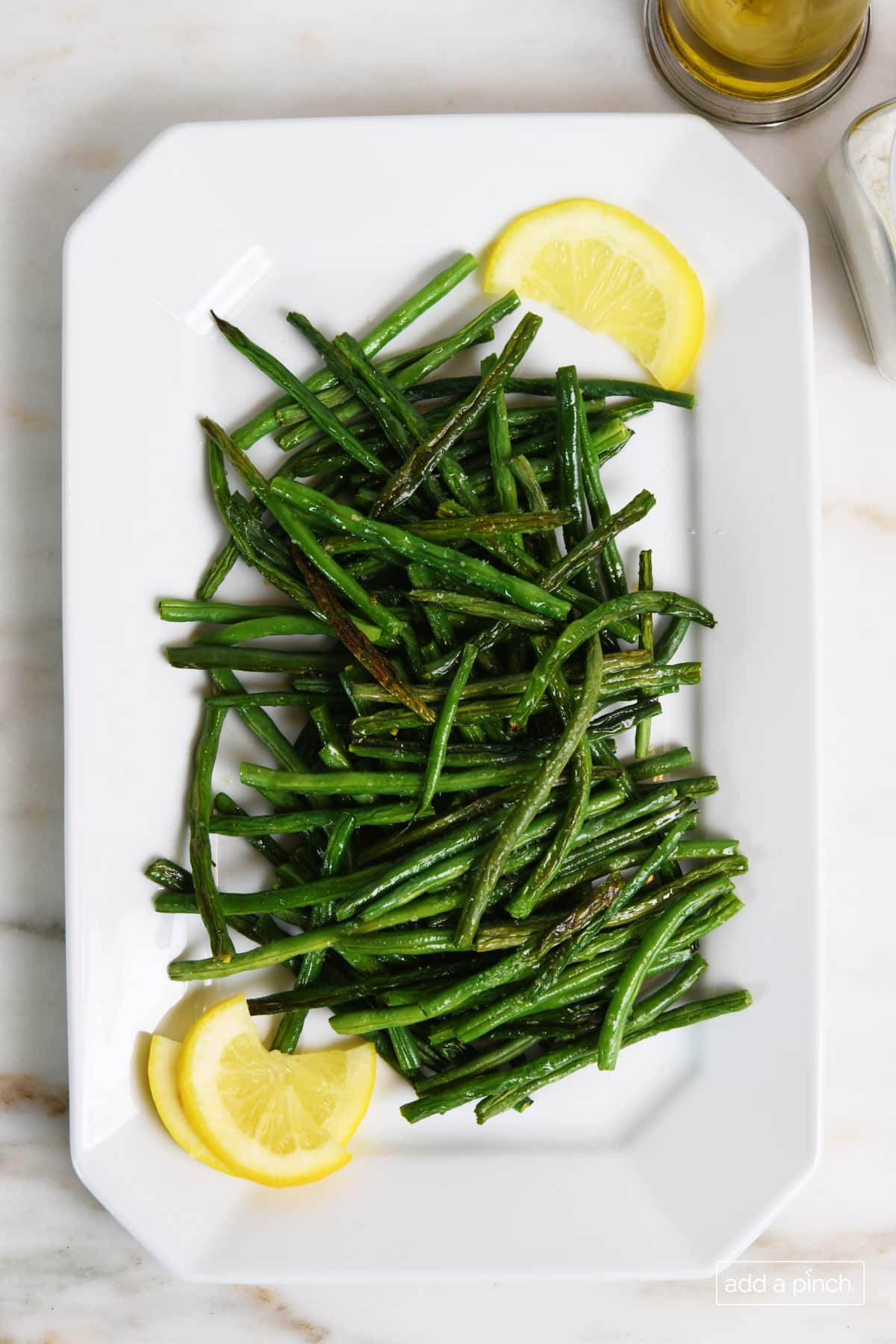 White serving tray holds roasted green beans and lemon wedges.