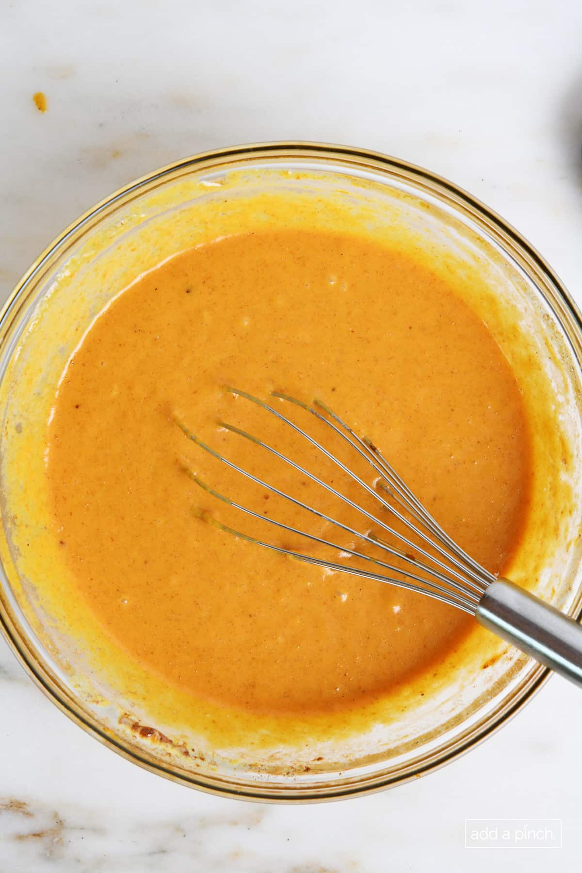 Combined pumpkin pie filling in a glass bowl with a whisk.