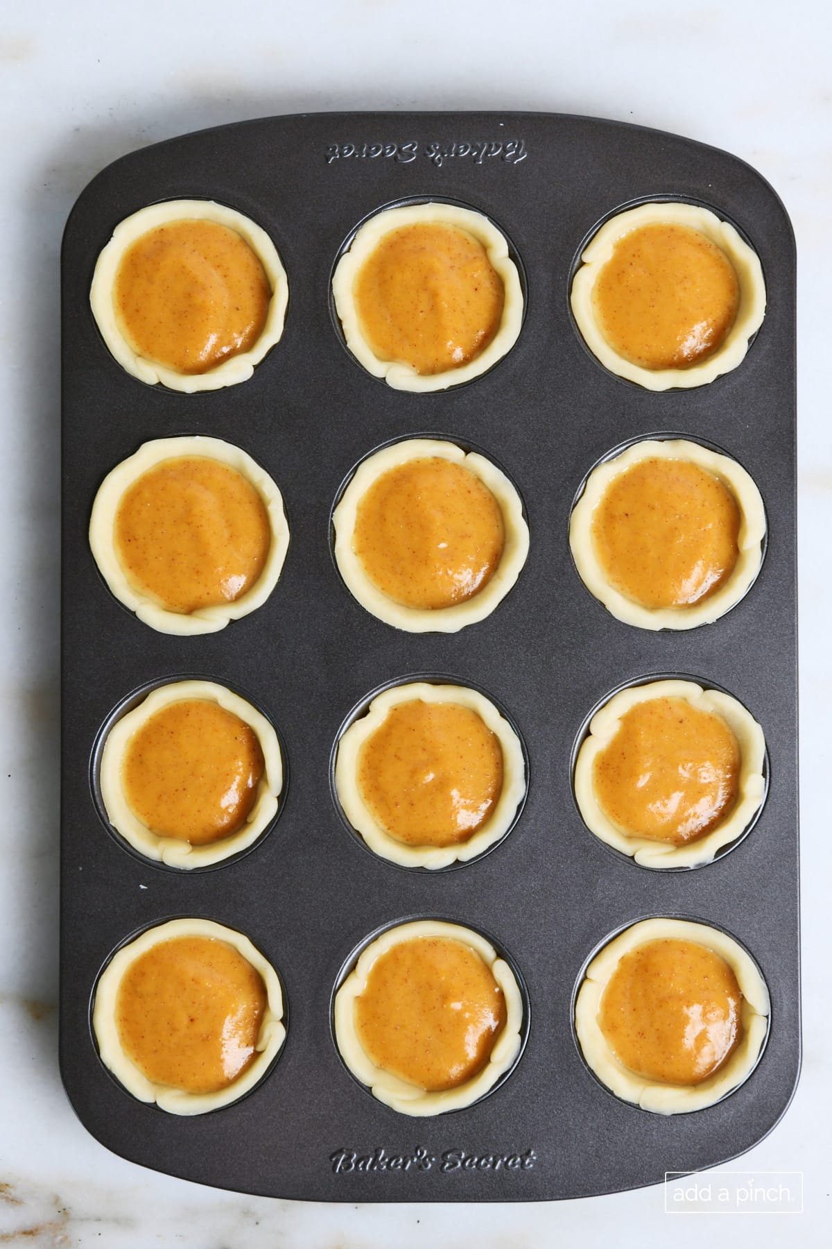 Pumpkin pie filling in a pastry dough in a mini muffin pan.