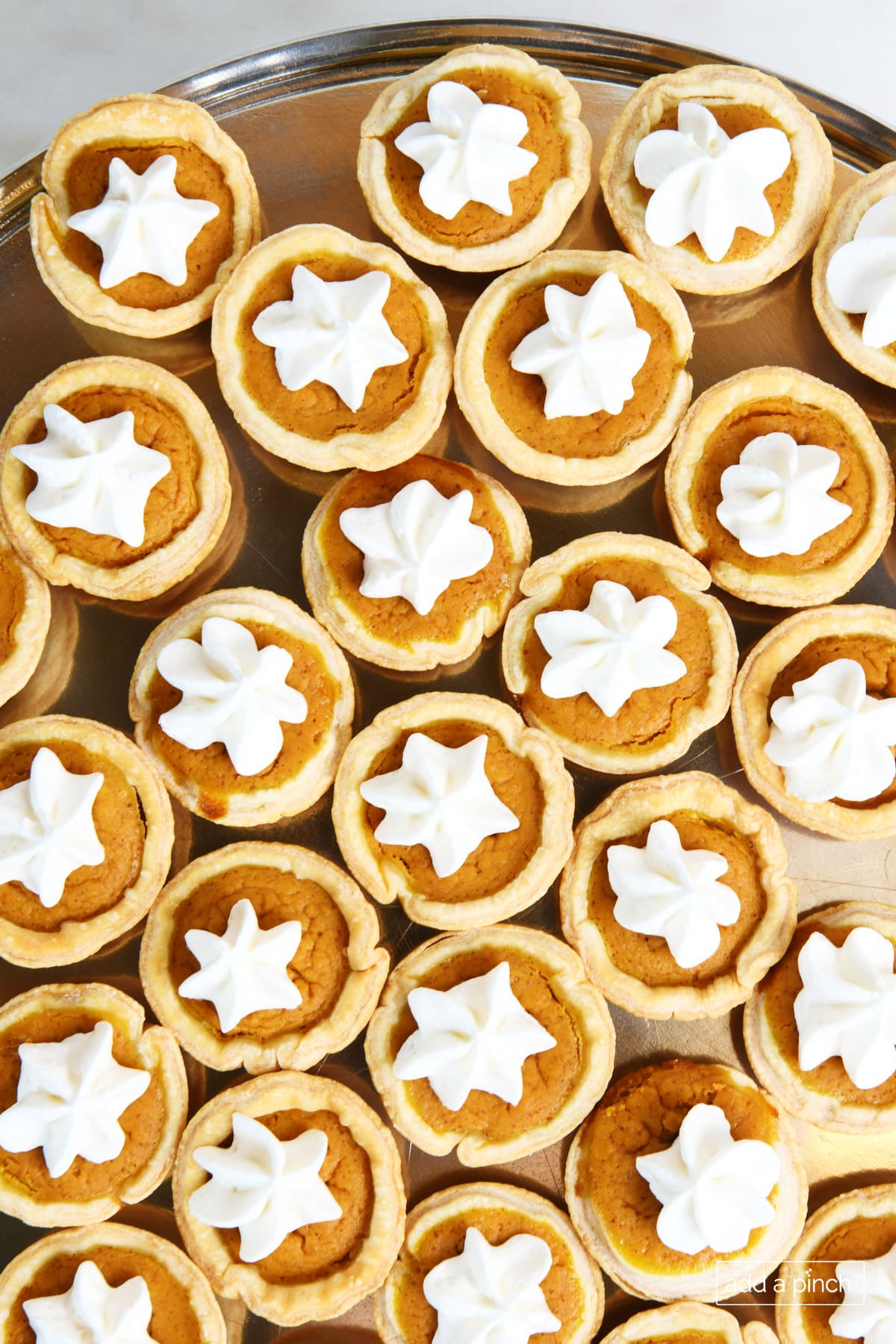 Mini pumpkin pie topped with whipped cream on a pewter plate.