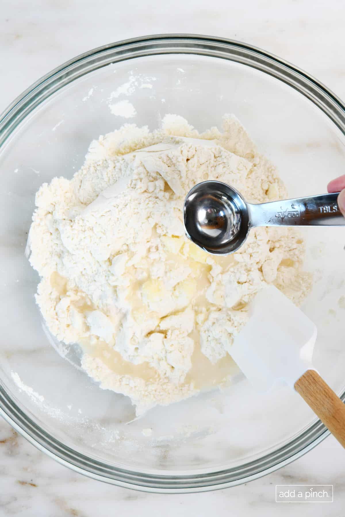 Adding ice water one tablespoon at a time to pie crust mixture and blending the mixture.