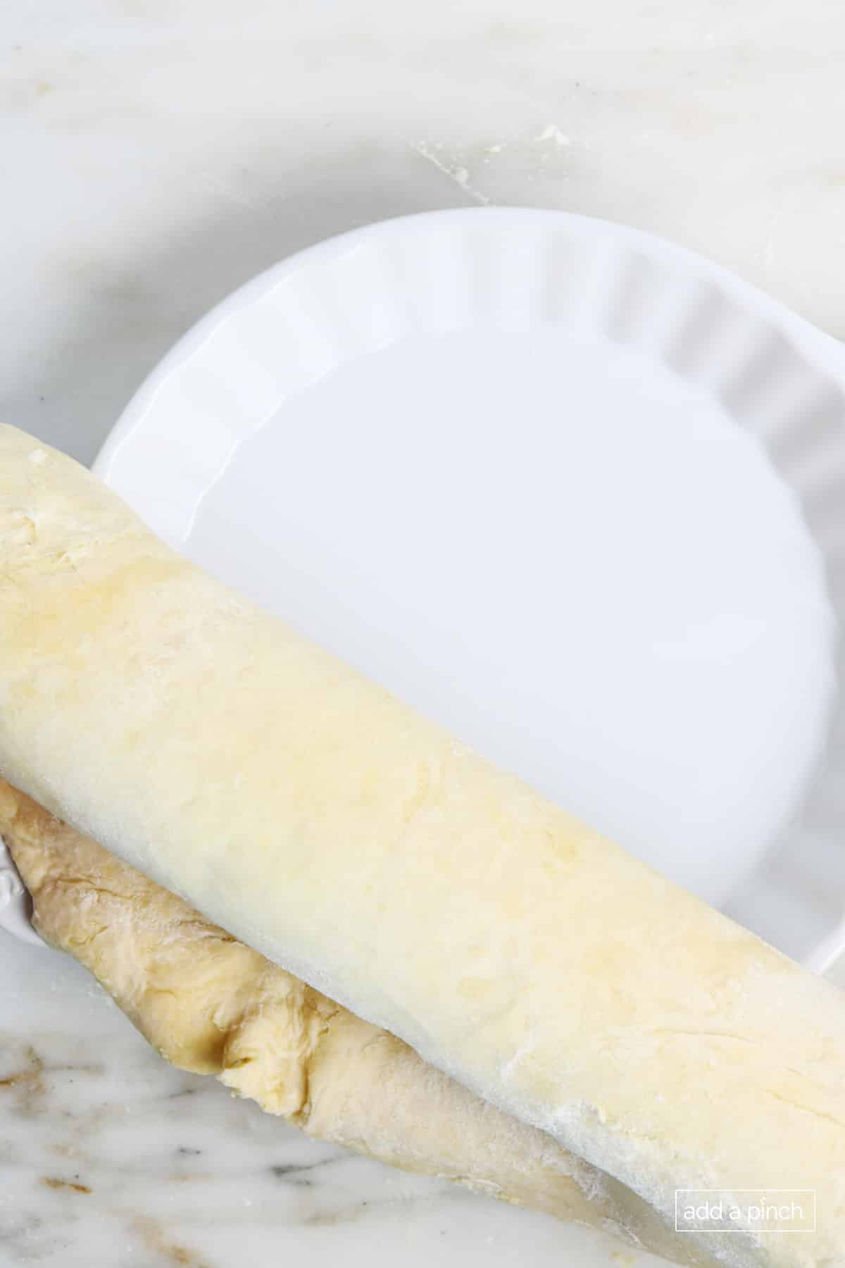 Pie dough laid over a pie plate and rolled over top with wooden rolling pin.