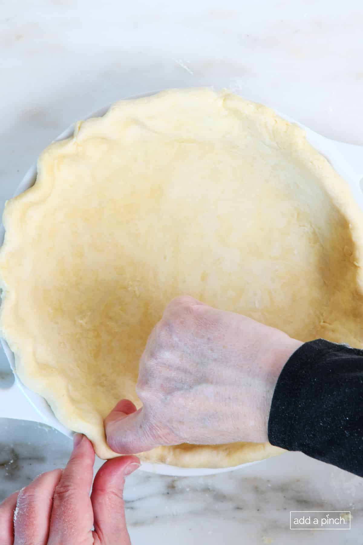 Pie dough in a pie dish that's being crimped around the edges with fingers. 