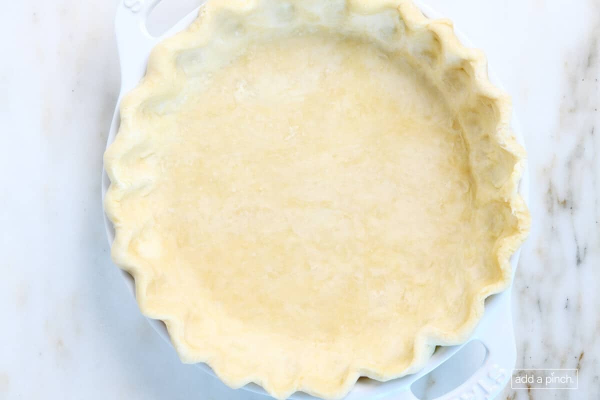 Pie dough that's been crimped and ready to bake sitting on a marble countertop.